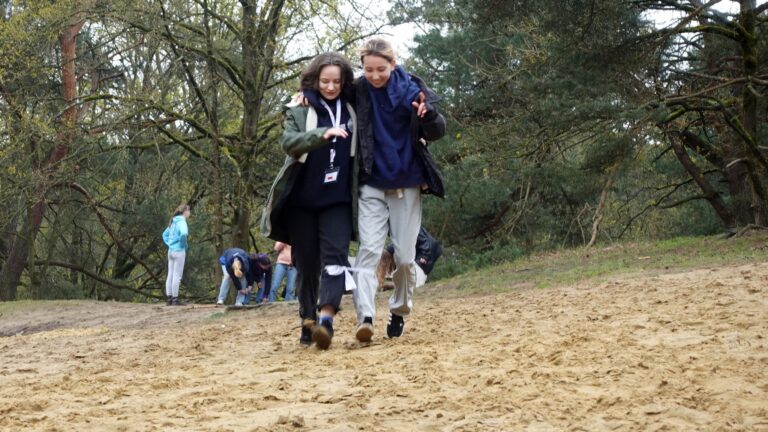 Dwie uczennice idą piaszczystą ścieżką. w tle uczniowie i drzewa.