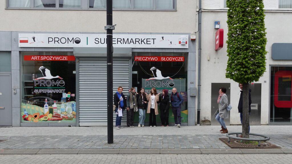 Uczniowie z nauczycielem stojący przed polskim supermarketem.